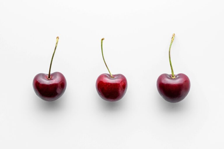 three cherries on a row on a white surface