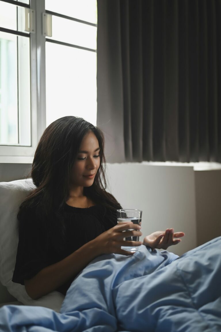 a woman holding a glass of water and consuming a capsule before bed